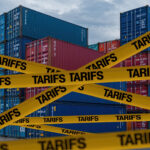 Symbolbild "Tariffs". American tariffs. Cargo Containers in Port with Yellow 'TARIFFS' Caution Tapes and American Flag Design, Overcast Sky Background. Copyright: Mohammad Xte - stock.adobe.com